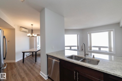 Kitchen peninsula featuring a double basin sink with a gooseneck faucet, light-toned countertop, and dark wood-finish cabinetry - 3104 10152 104 Street, Edmonton, AB - Indoor Photo Showing Kitchen With Double Sink