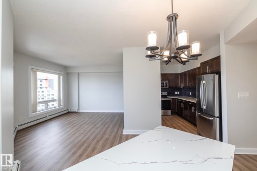 Open-concept living space featuring wood-finish flooring, a contemporary chandelier, a kitchen with dark cabinetry, stainless steel appliances, and white quartz countertops - 3104 10152 104 Street, Edmonton, AB - Indoor
