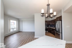 Open-concept living space featuring wood-finish flooring, a contemporary chandelier, a kitchen with dark cabinetry, stainless steel appliances, and white quartz countertops - 