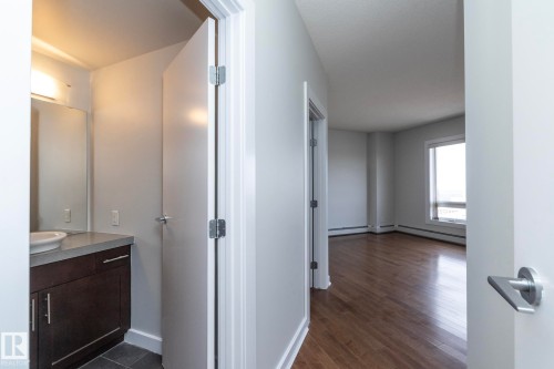 Entryway featuring a wood-finish floor leading into a bright room with a large window - 3104 10152 104 Street, Edmonton, AB - Indoor Photo Showing Other Room