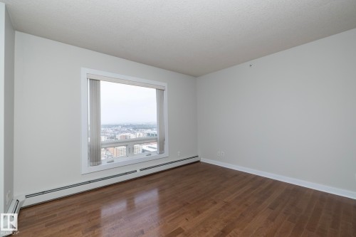 Spacious room featuring wood-finish flooring, white baseboards, and a large window with vertical blinds - 3104 10152 104 Street, Edmonton, AB - Indoor Photo Showing Other Room