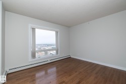 Spacious room featuring wood-finish flooring, white baseboards, and a large window with vertical blinds - 