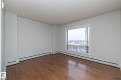 Expansive room featuring wood-finish flooring, a large window, a neutral color palette, and baseboard heating - 