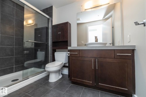 Modern bathroom featuring a glass-enclosed shower with dark tile surround, a dark wood-finish vanity with a vessel sink, a coordinating dark wood-finish storage cabinet, and large-format tile flooring - 3104 10152 104 Street, Edmonton, AB - Indoor Photo Showing Bathroom
