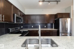 Contemporary kitchen featuring granite countertops, dark wood cabinetry with brushed nickel hardware, a stainless steel undermount sink with a high-arc faucet, stainless steel appliances, and a dark tile backsplash - 