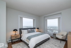 Bedroom featuring large windows, wood-finish flooring, light-colored walls, baseboard heating, and built-in window treatments - 