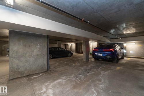 Concrete parking garage featuring exposed concrete columns and ceiling, overhead pipe work, and fluorescent strip lighting - 3104 10152 104 Street, Edmonton, AB - Indoor Photo Showing Garage
