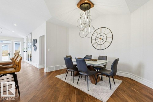 Dining area featuring vaulted ceilings, a contemporary chandelier, wood-finish flooring, a white dining table, and baseboard molding - 1 Sparrow Close, Fort Saskatchewan, AB - Indoor Photo Showing Dining Room