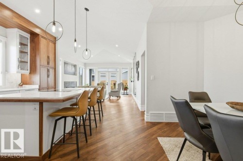 Kitchen and living area featuring wood-finish flooring, white cabinetry with display features, a kitchen island with seating, pendant lighting, and a vaulted ceiling - 1 Sparrow Close, Fort Saskatchewan, AB - Indoor Photo Showing Dining Room