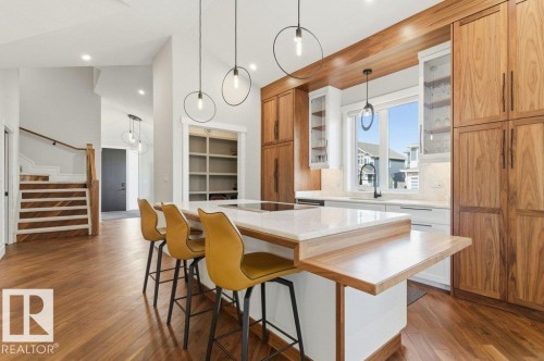Open-concept kitchen featuring wood-finish flooring, a central island with a light-toned countertop and breakfast bar, extensive wood-paneled cabinetry, and contemporary pendant lighting - 1 Sparrow Close, Fort Saskatchewan, AB - Indoor