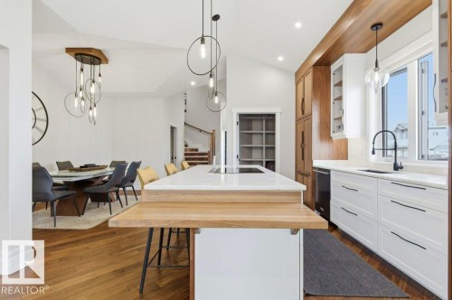 Open-concept kitchen featuring an island with a light wood-finish countertop extension, white shaker-style cabinetry, and a black matte faucet - 1 Sparrow Close, Fort Saskatchewan, AB - Indoor Photo Showing Other Room