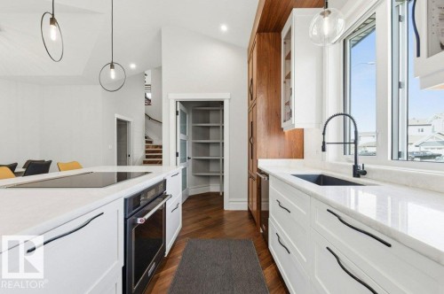 Modern kitchen featuring an integrated cooktop on the island, white cabinetry with contemporary hardware, and wood-finish flooring - 1 Sparrow Close, Fort Saskatchewan, AB - Indoor Photo Showing Kitchen With Upgraded Kitchen