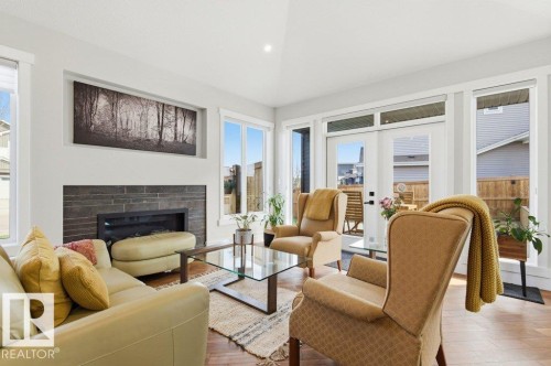 Living area featuring a modern linear fireplace with stacked stone surround, multiple large windows, and patio door access to the exterior - 1 Sparrow Close, Fort Saskatchewan, AB - Indoor Photo Showing Living Room With Fireplace