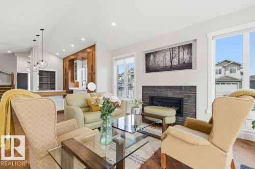 Bright living area featuring wood-finish flooring, a contemporary fireplace with a stone surround, and large windows - 1 Sparrow Close, Fort Saskatchewan, AB - Indoor Photo Showing Living Room With Fireplace