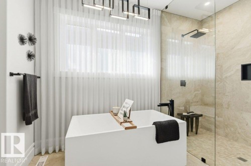 Contemporary bathroom featuring a freestanding tub, glass-enclosed shower, rain shower head, large window with sheer drapes, and stone-finish wall tile - 1 Sparrow Close, Fort Saskatchewan, AB - Indoor Photo Showing Bathroom