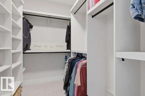 Spacious walk-in closet featuring built-in shelving, multiple hanging rods, white-finish cabinetry, and neutral-tone carpeting - 1 Sparrow Close, Fort Saskatchewan, AB - Indoor With Storage