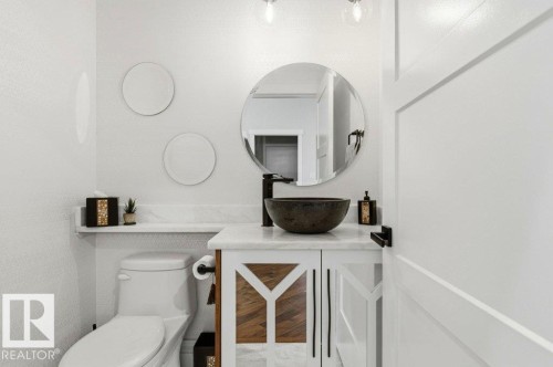 Bathroom featuring a wood-finish vanity with a vessel sink, quartz countertop, and round mirror - 1 Sparrow Close, Fort Saskatchewan, AB - Indoor Photo Showing Other Room