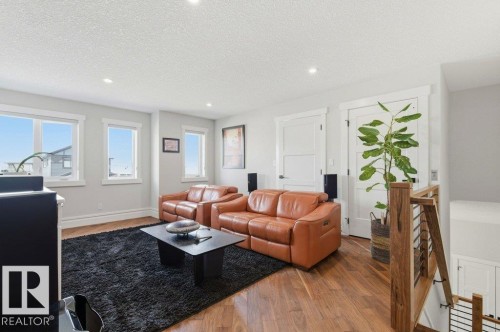Light-filled living area featuring wood-finish flooring, recessed lighting, multiple windows, and a modern wood and metal staircase railing - 1 Sparrow Close, Fort Saskatchewan, AB - Indoor Photo Showing Living Room