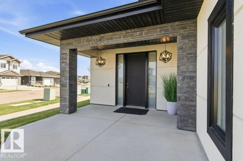 Covered front porch featuring stacked stone accents, a dark entry door, and geometric pendant lighting - 1 Sparrow Close, Fort Saskatchewan, AB - Outdoor With Exterior