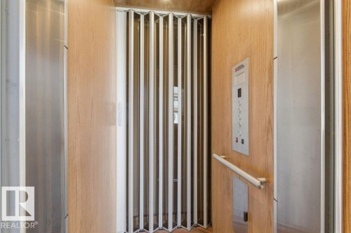 Residential elevator featuring wood-finish paneling, an accordion safety gate, a polished stainless steel control panel, a horizontal handrail, and brushed metal accent panels - 1 Sparrow Close, Fort Saskatchewan, AB - Indoor