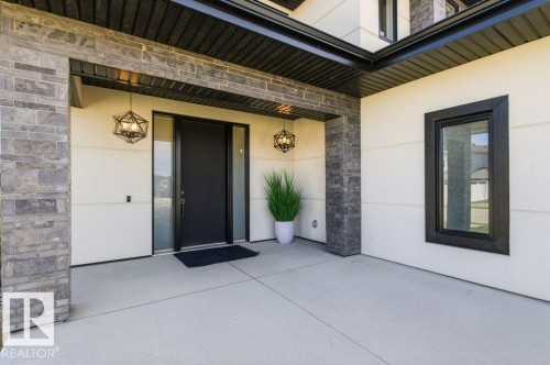 Covered entry featuring a modern black door with sidelights, stone-clad pillars, and two geometric pendant lights - 1 Sparrow Close, Fort Saskatchewan, AB - Outdoor With Exterior