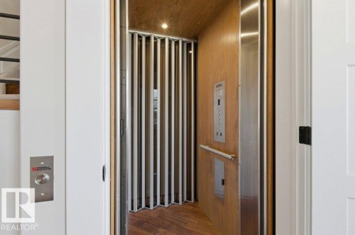 In-home elevator featuring wood-finish flooring, wood-paneled walls, and a stainless steel control panel - 1 Sparrow Close, Fort Saskatchewan, AB - Indoor Photo Showing Other Room