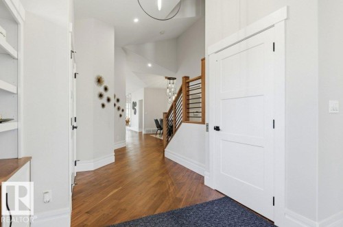 Entryway featuring wood-finish flooring, a contemporary staircase with wooden handrail and black metal balusters, built-in shelving, white trim, and a white interior door with black hardware - 1 Sparrow Close, Fort Saskatchewan, AB - Indoor Photo Showing Other Room