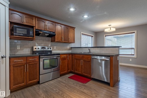 Kitchen featuring wood-finish flooring, cherry wood cabinetry, and stainless steel appliances - 17715 6 Avenue, Edmonton, AB - Indoor Photo Showing Kitchen With Stainless Steel Kitchen With Double Sink