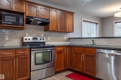 Kitchen featuring rich wood cabinetry, stainless steel appliances, dark countertops, a subway tile backsplash, and wood-finish flooring - 