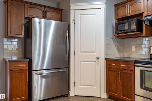 Kitchen featuring wood cabinetry, dark countertops, a stainless steel refrigerator, and a light-toned tile backsplash - 17715 6 Avenue, Edmonton, AB - Indoor Photo Showing Kitchen With Stainless Steel Kitchen