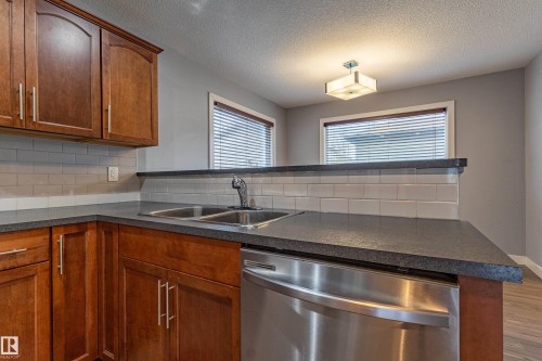 Kitchen featuring rich wood cabinetry, stone-finish countertops, and a subway tile backsplash - 17715 6 Avenue, Edmonton, AB - Indoor Photo Showing Kitchen With Double Sink