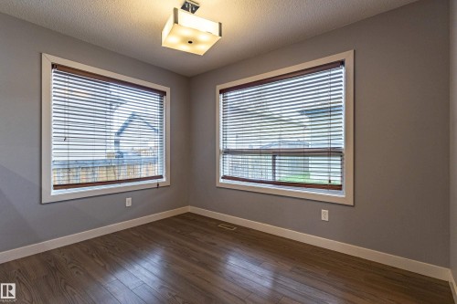 Room featuring wood-finish flooring, two windows with blinds, and a contemporary ceiling light fixture - 17715 6 Avenue, Edmonton, AB - Indoor Photo Showing Other Room