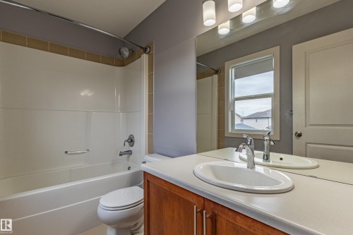 Bathroom featuring a vanity with a white countertop and wood-finish cabinetry, an oval undermount sink with a chrome faucet, and an expansive mirror - 17715 6 Avenue, Edmonton, AB - Indoor Photo Showing Bathroom