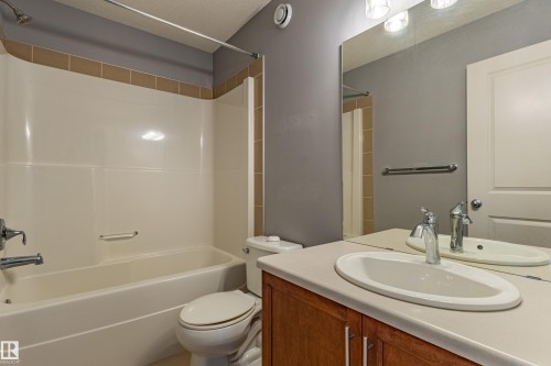 Bathroom featuring a full-size bathtub with integrated shower, single vanity with oval sink, large wall-mounted mirror, and wood-finish cabinetry - 17715 6 Avenue, Edmonton, AB - Indoor Photo Showing Bathroom