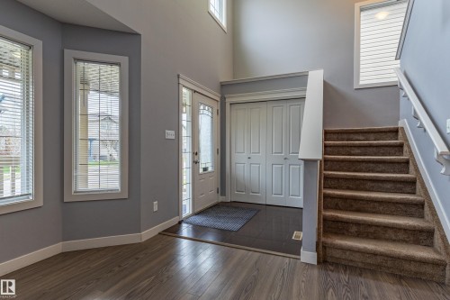 Entryway featuring wood-finish flooring, a carpeted staircase with white handrails, a front door with decorative glass inserts, and a coat closet with bi-fold doors - 17715 6 Avenue, Edmonton, AB - Indoor Photo Showing Other Room