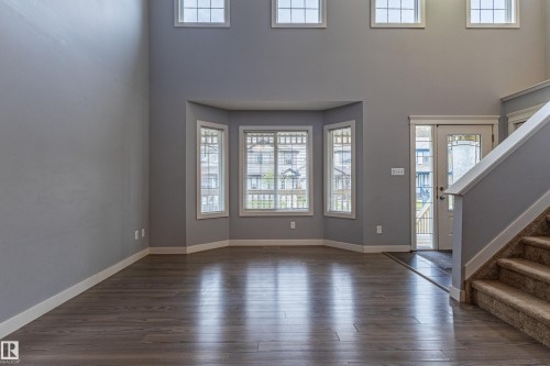 Two-story foyer featuring wood-finish flooring, a bay window with multiple panes, and a staircase with carpeted treads and a white balustrade - 17715 6 Avenue, Edmonton, AB - Indoor Photo Showing Other Room
