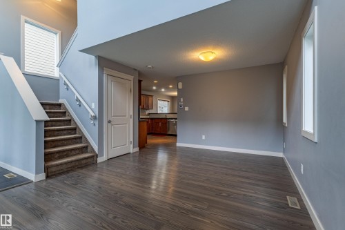 Open concept living area featuring wood-finish flooring, a carpeted staircase with white railing, and multiple windows providing natural illumination - 17715 6 Avenue, Edmonton, AB - Indoor Photo Showing Other Room