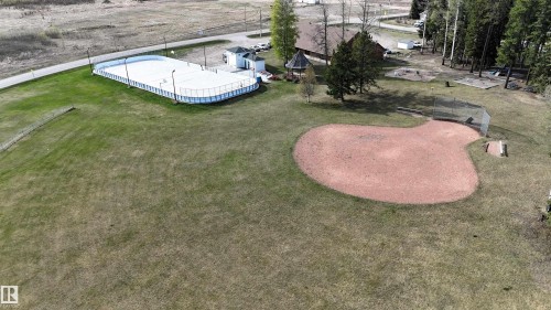 Expansive green space featuring a baseball diamond, an outdoor rink with boards, a small white utility building, and a wooded area - 7126 4A Ave, Edson, AB - Outdoor