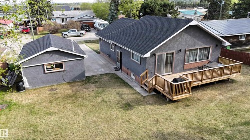 Rear exterior featuring a spacious wood-finish deck with railings, a sliding glass door, and a detached structure with a window and a shingle roof - 7126 4A Ave, Edson, AB - Outdoor