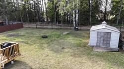 Expansive backyard featuring a wood deck, a white storage shed, a fire pit area, and a tree-lined perimeter - 
