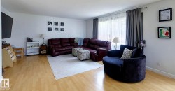 Spacious living area featuring light wood-finish flooring, a neutral color palette, and large windows with sheer and blackout drapes - 
