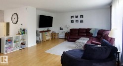 Open-concept living space featuring wood-finish flooring, white walls, and bright natural light from a large window - 