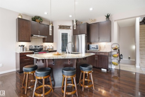 Spacious kitchen featuring dark wood cabinetry, stainless steel appliances, granite countertops, a large island with seating, and dark wood-finish flooring - 1444 37C Avenue, Edmonton, AB - Indoor Photo Showing Kitchen With Upgraded Kitchen