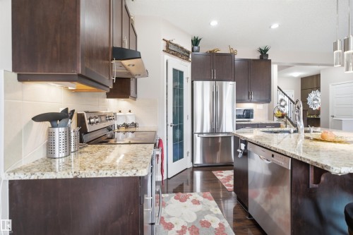 Kitchen featuring dark wood cabinetry, light-toned stone countertops, stainless steel appliances, and wood-finish flooring - 1444 37C Avenue, Edmonton, AB - Indoor Photo Showing Kitchen With Upgraded Kitchen