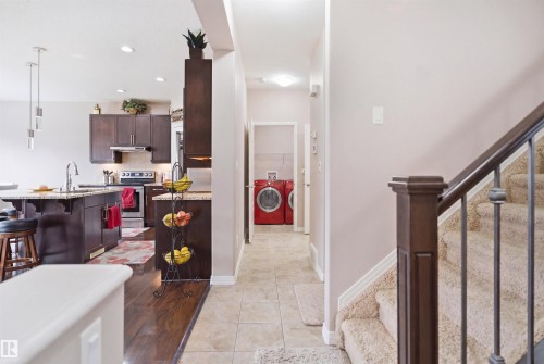 Kitchen featuring dark wood cabinetry, stainless steel appliances, a center island with sink and granite-style countertop, and wood-finish flooring - 1444 37C Avenue, Edmonton, AB - Indoor