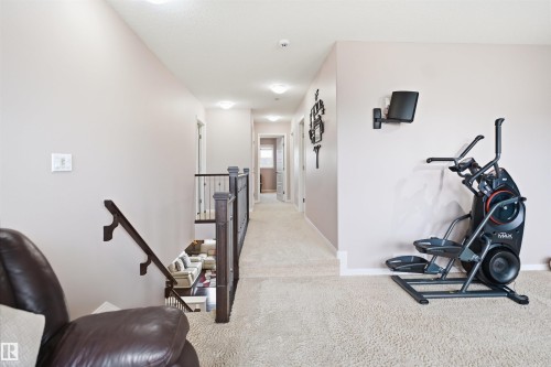 Carpeted upper-level hallway featuring a dark wood handrail and balusters overlooking a lower level - 1444 37C Avenue, Edmonton, AB - Indoor Photo Showing Gym Room