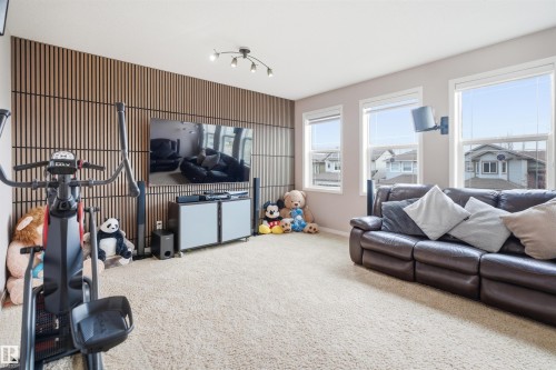Spacious room featuring accent paneling, overhead track lighting, multiple windows, and light-colored carpet flooring - 1444 37C Avenue, Edmonton, AB - Indoor