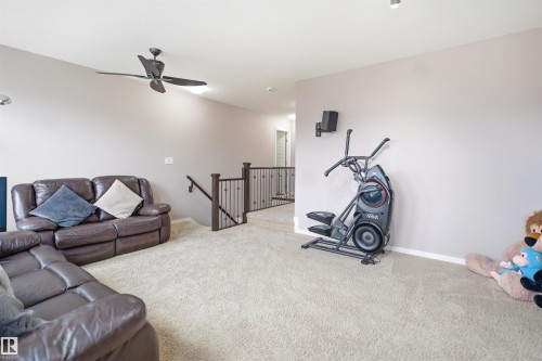 Carpeted secondary living space featuring a ceiling fan, recessed lighting, and a wood-finish handrail with wrought iron balusters - 1444 37C Avenue, Edmonton, AB - Indoor Photo Showing Gym Room