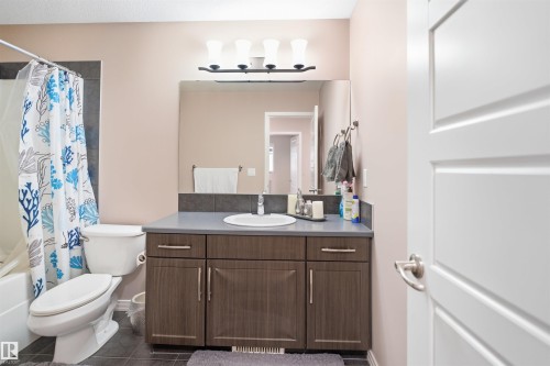 Modern bathroom featuring a wood-finish vanity with a single basin, a large mirror, and contemporary light fixture - 1444 37C Avenue, Edmonton, AB - Indoor Photo Showing Bathroom