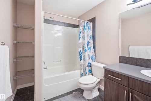 Bathroom featuring a white tub/shower combination with dark tile surround, a dark wood-finish vanity with a light gray countertop and integrated sink, and an overhead vanity light fixture - 1444 37C Avenue, Edmonton, AB - Indoor Photo Showing Bathroom